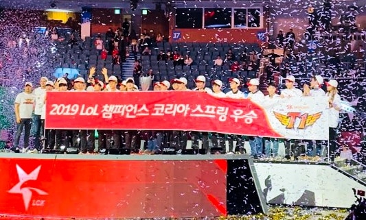 The esports team SKT celebrate on stage with a banner that contains Korean lettering after winning the 2019 LCK Spring Finals