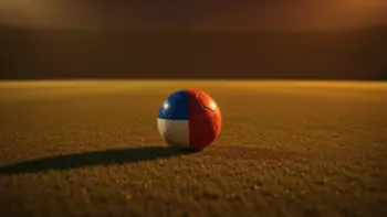 Empty floodlit football pitch at dusk with ball on penalty spot, orange and blue lighting tones.