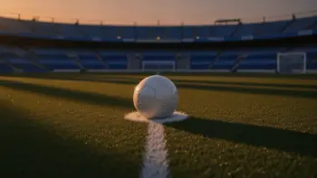 Empty floodlit football pitch with ball on penalty spot, green and blue stadium lighting, dusk atmosphere.