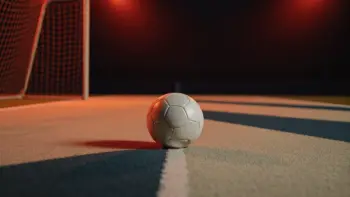 Floodlit football pitch with ball on centre spot, dramatic evening stadium lighting, shallow depth of field.