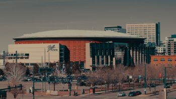 Ball Arena's curved roof and red facade in downtown Denver, with bare trees in front