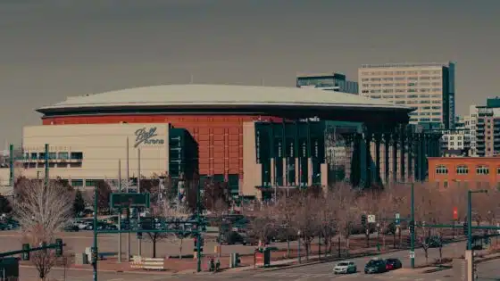 Ball Arena's curved roof and red facade in downtown Denver, with bare trees in front
