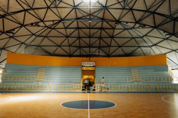 Empty indoor basketball court under a geometric domed roof, one person jogging past