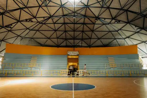 Empty indoor basketball court under a geometric domed roof, one person jogging past