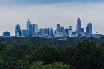 Charlotte's uptown skyline rising above a dense band of green trees under cloudy skies